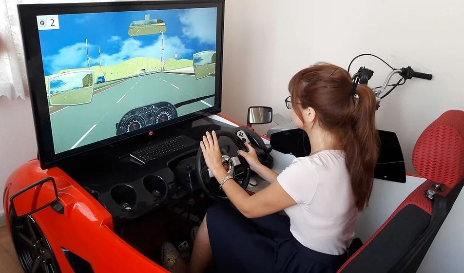 Bir kursiyer sürüş simülatöründe direksiyon eğitimi alıyor
